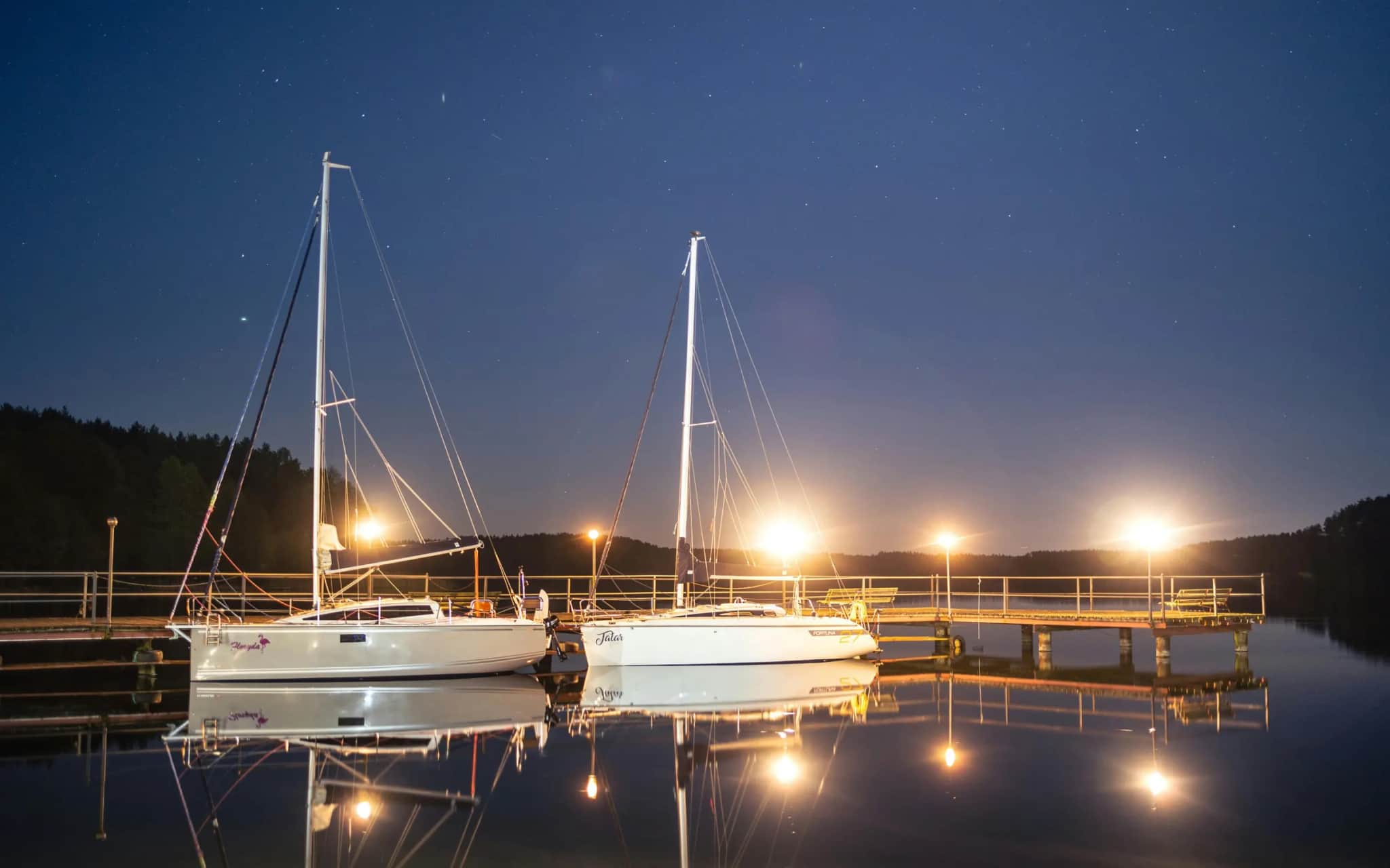 Czarter jachtów na Mazurach — żaglówki przy pomoście nocą pod rozgwieżdżonym niebem nad mazurskim jeziorem